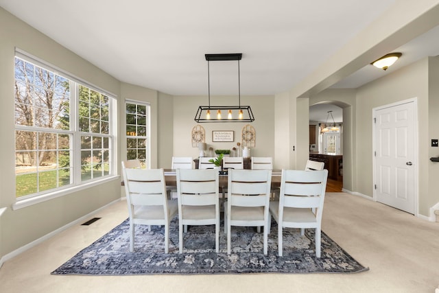 dining space featuring arched walkways, baseboards, visible vents, and light colored carpet