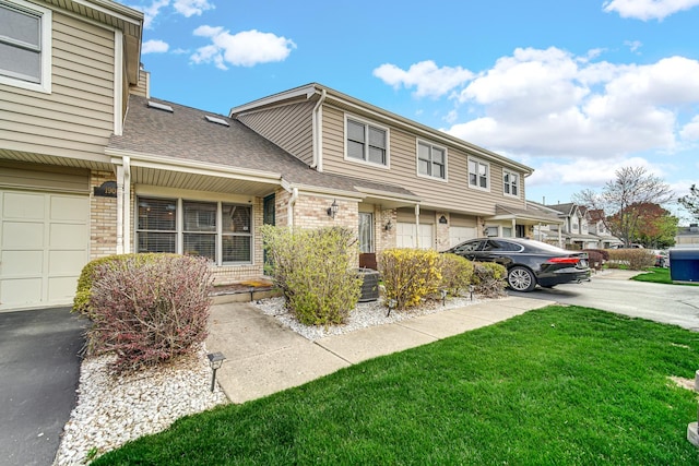 multi unit property featuring a garage, brick siding, a front lawn, driveway, and roof with shingles