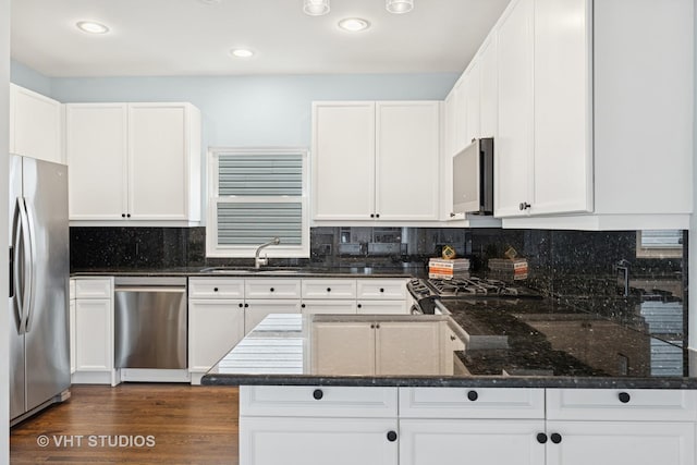 kitchen featuring white cabinetry, a sink, dark stone countertops, backsplash, and stainless steel appliances