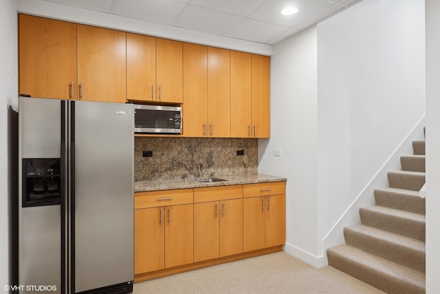 kitchen with light stone countertops, tasteful backsplash, light carpet, a sink, and stainless steel appliances