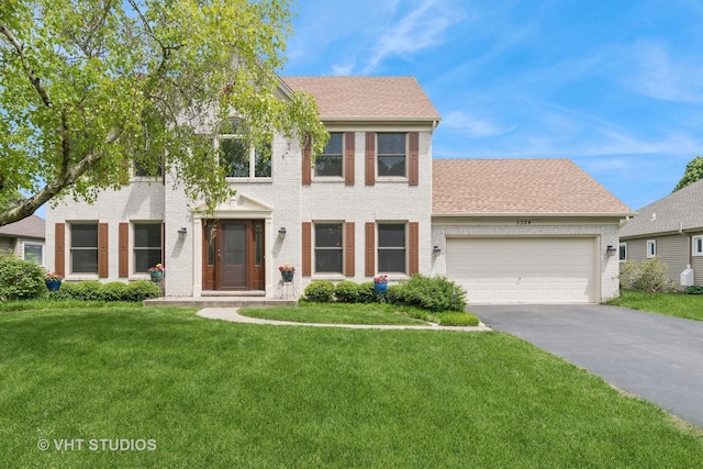 colonial inspired home with brick siding, driveway, an attached garage, and a front lawn