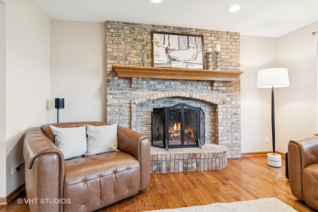 living room with wood finished floors, baseboards, a brick fireplace, and recessed lighting