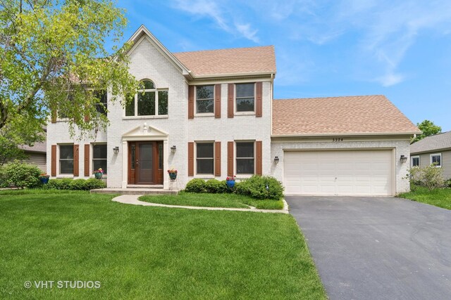 colonial-style house featuring brick siding, asphalt driveway, a garage, and a front yard