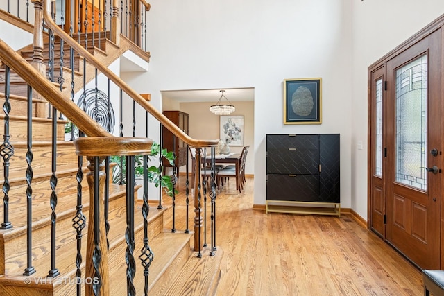 entrance foyer with a towering ceiling, stairs, light wood finished floors, healthy amount of natural light, and baseboards