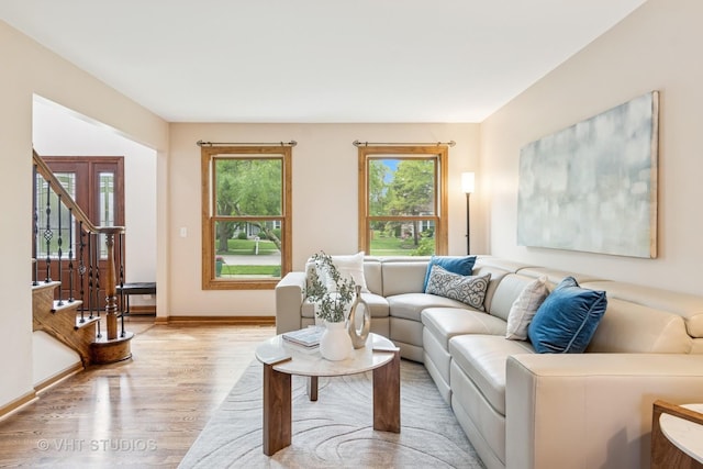 living room featuring light wood finished floors, baseboards, and stairs