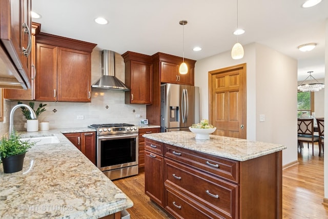 kitchen with appliances with stainless steel finishes, wall chimney exhaust hood, a sink, light wood finished floors, and decorative backsplash