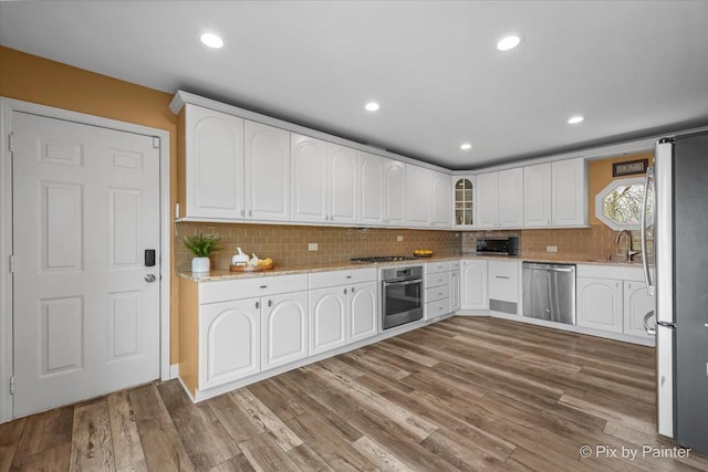 kitchen featuring decorative backsplash, wood finished floors, glass insert cabinets, stainless steel appliances, and white cabinetry