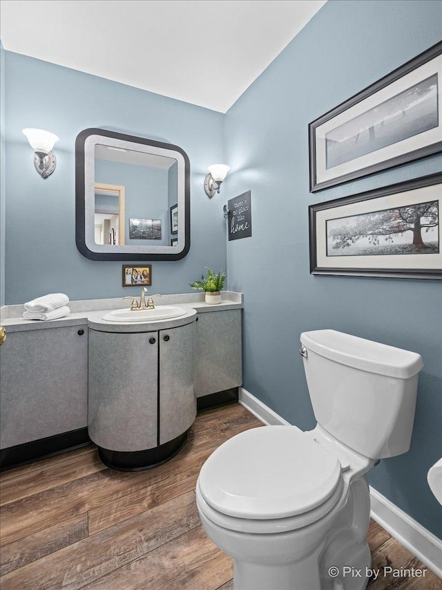 half bathroom with vanity, baseboards, toilet, and wood finished floors