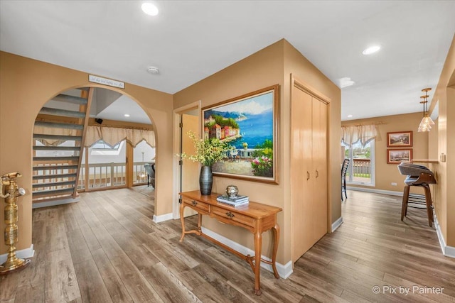 corridor featuring baseboards, arched walkways, and wood finished floors
