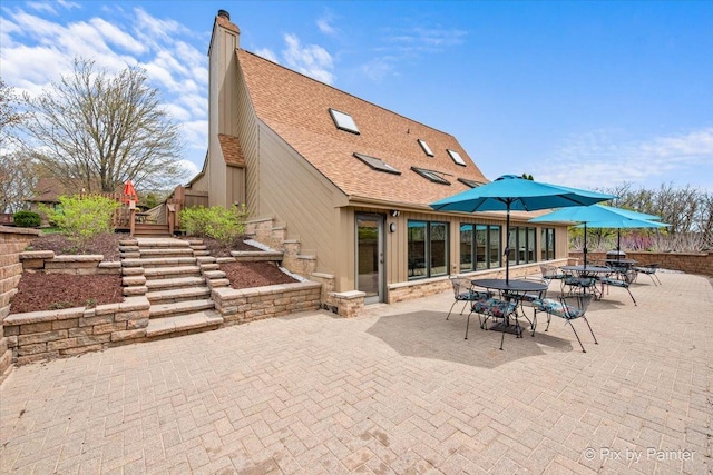 back of house with outdoor dining area, a chimney, a shingled roof, a patio area, and stairway