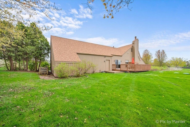 rear view of property featuring roof with shingles, a chimney, a yard, and a deck