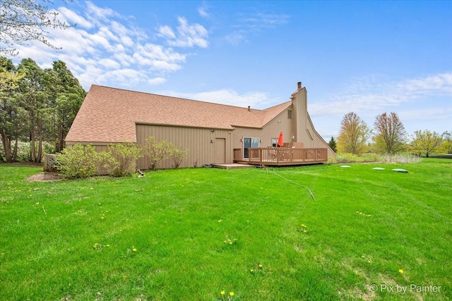 back of property with a lawn, a wooden deck, a shingled roof, and a chimney