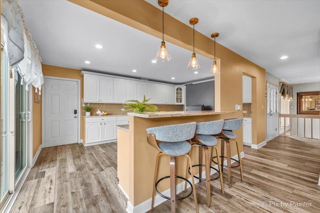 kitchen with light wood-style flooring, backsplash, white cabinetry, and a kitchen bar