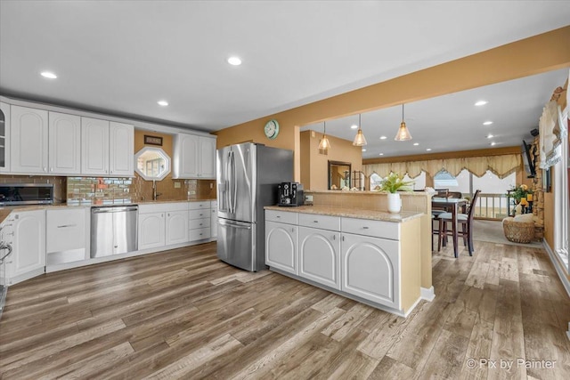 kitchen featuring light wood-style floors, stainless steel appliances, white cabinetry, a peninsula, and tasteful backsplash