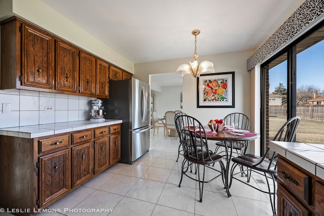 kitchen featuring a chandelier, tile countertops, decorative backsplash, freestanding refrigerator, and hanging light fixtures