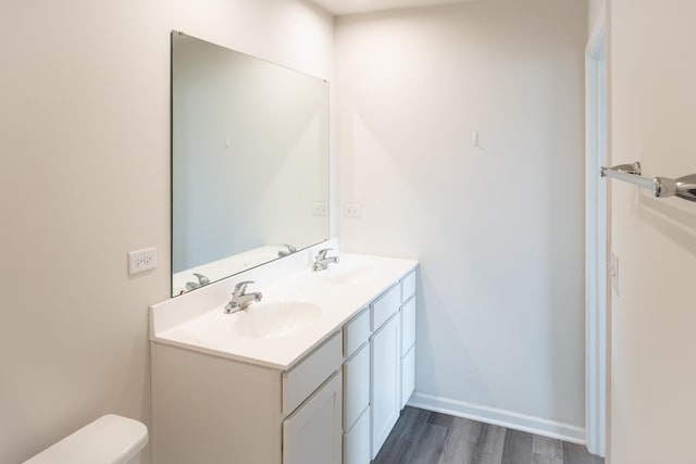 bathroom featuring double vanity, toilet, wood finished floors, and a sink