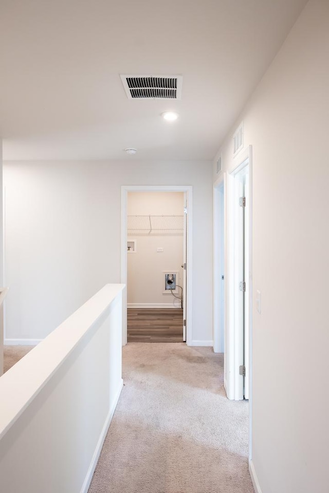 hall with baseboards, an upstairs landing, visible vents, and light colored carpet