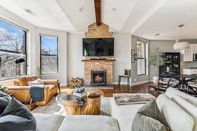 living room with visible vents, vaulted ceiling with beams, baseboards, a fireplace, and wood finished floors