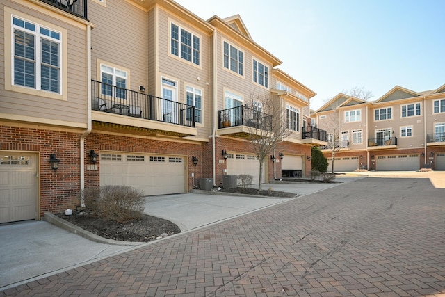 view of property featuring central AC, brick siding, an attached garage, driveway, and a residential view