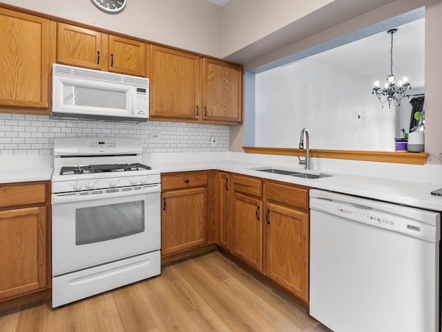 kitchen with white appliances, brown cabinetry, light countertops, light wood finished floors, and a sink