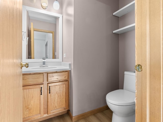 half bathroom featuring wood finished floors, toilet, vanity, and baseboards