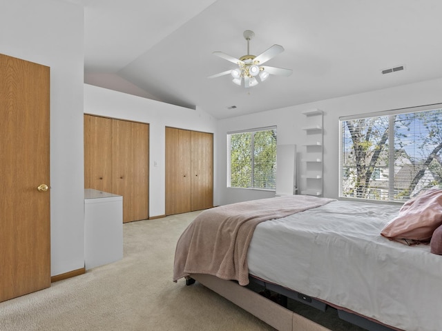 bedroom with two closets, a ceiling fan, visible vents, light carpet, and lofted ceiling