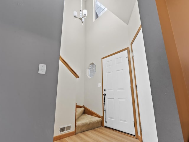 entrance foyer with an inviting chandelier, stairs, light wood-type flooring, visible vents, and a towering ceiling