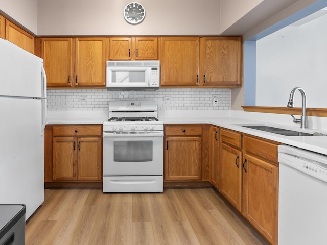 kitchen featuring light wood finished floors, a sink, brown cabinets, and white appliances