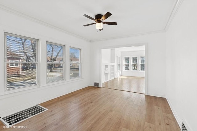 empty room featuring crown molding, wood finished floors, visible vents, and a healthy amount of sunlight