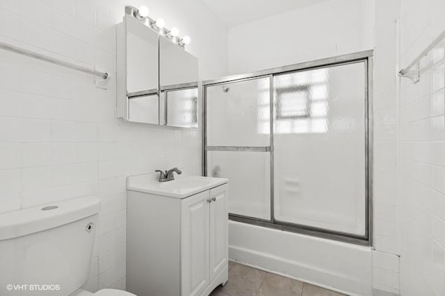 bathroom with vanity, shower / bath combination with glass door, tile walls, toilet, and tile patterned floors