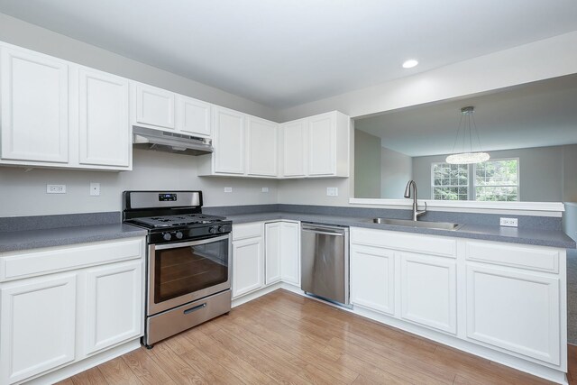 kitchen featuring a peninsula, a sink, stainless steel appliances, white cabinets, and under cabinet range hood