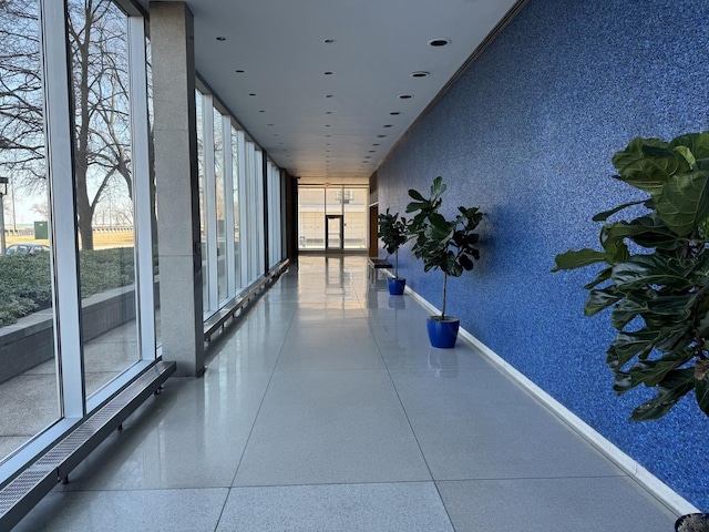 hall with wallpapered walls, baseboards, and expansive windows