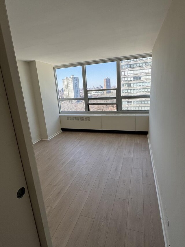 unfurnished room with light wood-style flooring, a view of city, and baseboards