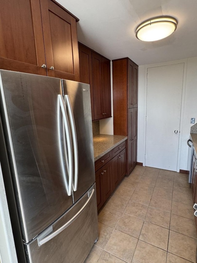 kitchen with stone counters, light tile patterned flooring, and freestanding refrigerator