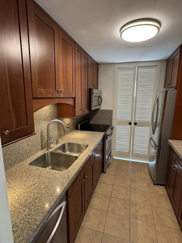 kitchen with backsplash, light tile patterned floors, light stone counters, appliances with stainless steel finishes, and a sink