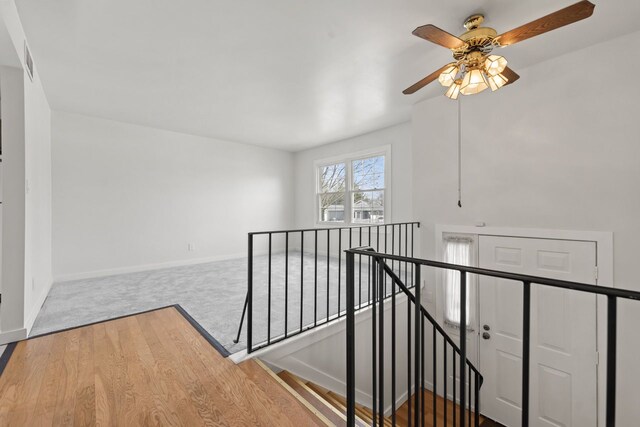 hallway with an upstairs landing, visible vents, carpet floors, and baseboards