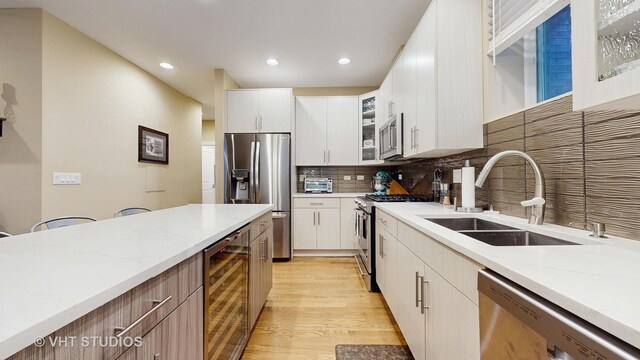 kitchen with appliances with stainless steel finishes, tasteful backsplash, a sink, beverage cooler, and light wood-style floors