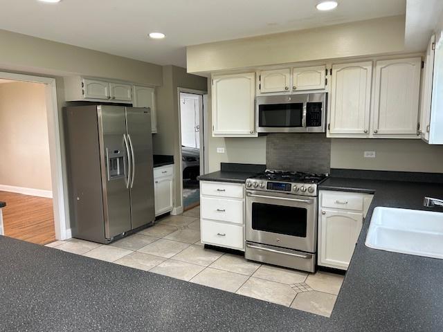 kitchen featuring a sink, light tile patterned floors, stainless steel appliances, and dark countertops