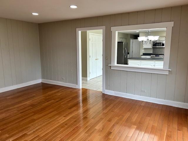 unfurnished living room featuring baseboards, an inviting chandelier, and hardwood / wood-style floors