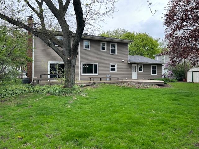 back of property featuring a storage shed, a wooden deck, an outbuilding, a patio area, and a yard