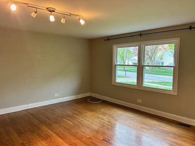 unfurnished room with baseboards, wood finished floors, visible vents, and track lighting