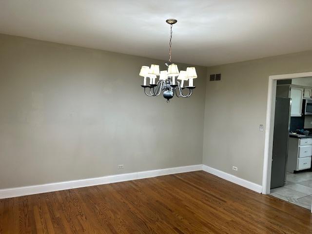 spare room featuring baseboards, a notable chandelier, wood finished floors, and visible vents