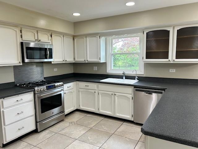 kitchen featuring light tile patterned floors, dark countertops, appliances with stainless steel finishes, and a sink