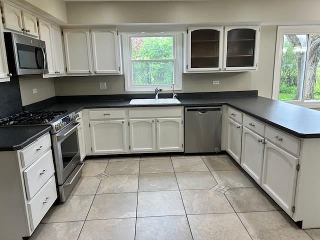 kitchen with a peninsula, dark countertops, a sink, appliances with stainless steel finishes, and light tile patterned floors