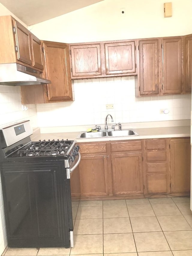 kitchen featuring tasteful backsplash, vaulted ceiling, under cabinet range hood, stainless steel gas stove, and a sink