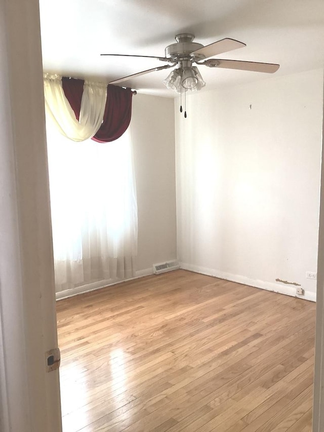 spare room with light wood finished floors, baseboards, visible vents, and ceiling fan