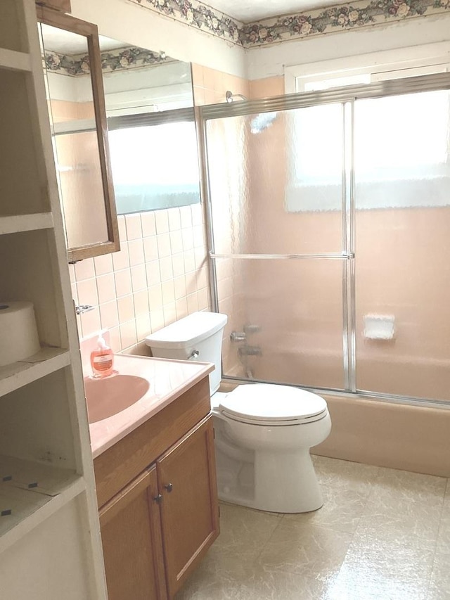 bathroom featuring vanity, tile walls, toilet, backsplash, and enclosed tub / shower combo