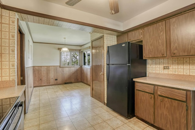 kitchen with freestanding refrigerator, light countertops, brown cabinetry, and a wainscoted wall