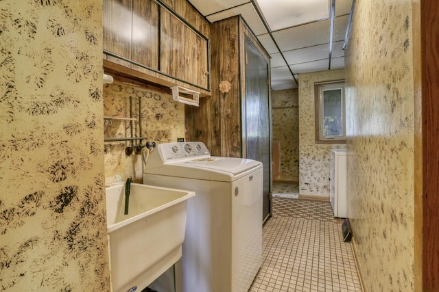 clothes washing area with tile patterned flooring, washer / dryer, wallpapered walls, a sink, and cabinet space