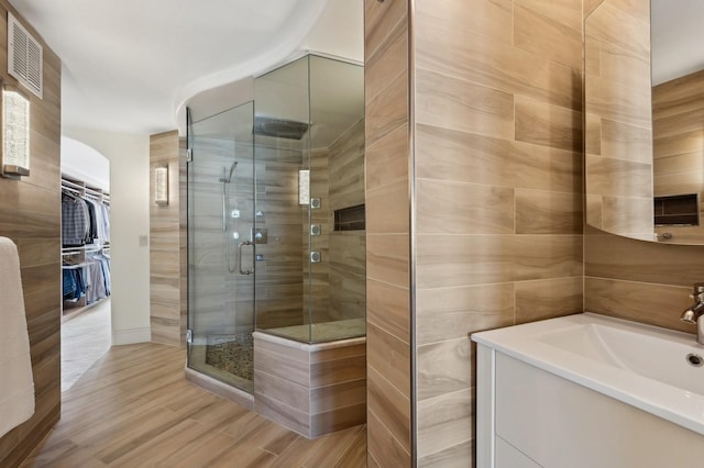 bathroom featuring visible vents, a shower stall, a walk in closet, tile walls, and a sink